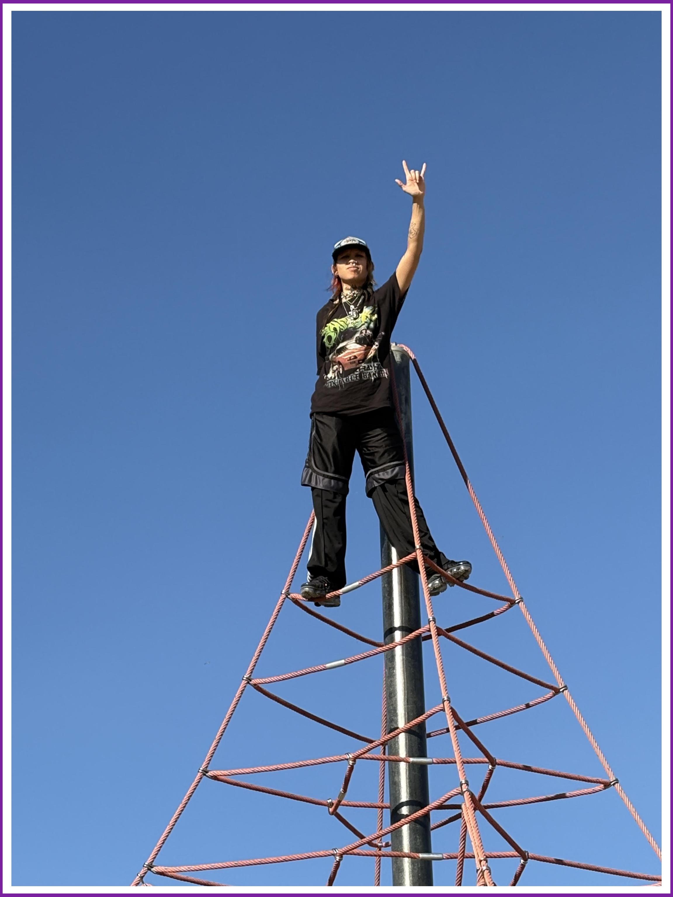 Image Description: Lawu raising a rock-and-roll hand sign atop a playground structure.